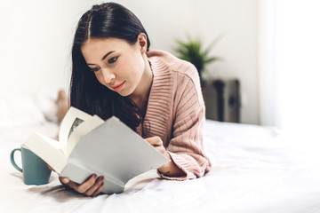 Young woman relaxing and reading book on bed at home