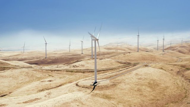 Aerial. 4K. The view of a number of windwills producing renewal electric energy in California, USA. Clear blue sky and golden hills are all around.