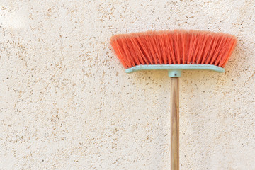 A used plastic red broom leans with bristles facing up on a plastered wall with text box