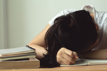 teenager holding pencil and lying  sleeping on desk with book and homework.