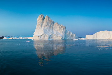 Fototapeta na wymiar Iceberg at sunset. Nature and landscapes of Greenland. Disko bay. West Greenland. Summer Midnight Sun and icebergs. Big blue ice in icefjord. Affected by climate change and global warming.