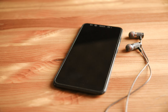 Black headphones and smartphone lies on wooden background. Design layout, smart phone with black screen and wired headphones with copy space.