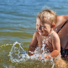 Carefree child plays in the water in her mother’s arms