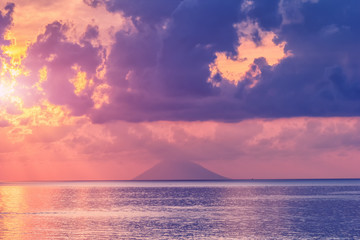 Sea landscape with view on Stromboli volcano island in haze. Evening sunlight and clouds