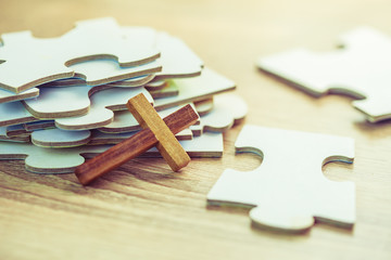 Close up of wooden cross over white jigsaw puzzle on wooden desk background, Christian concept show...