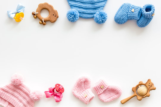 Blue and pink knitted footwear, hat, dummy, rattle frame for baby on white background top view mockup