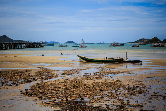 Small wooden fishing boats mooring at the dirty beach in front of fisherman village in Thailand on the sunny day
