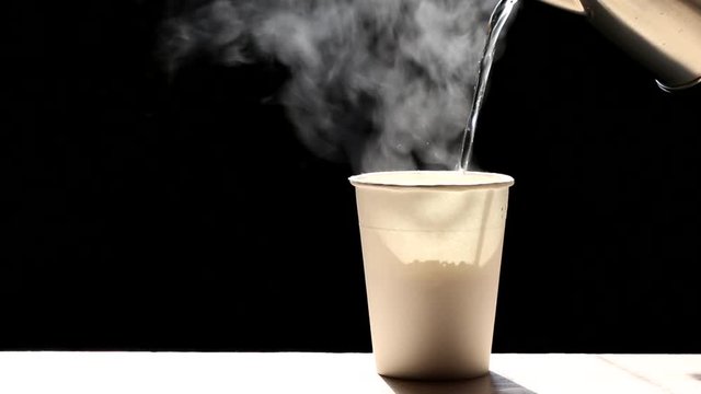 Woman pouring hot water into instant noodles in cup with smoke rising and garlic on dark background, Sodium diet high risk kidney failure, Healthy eating concept