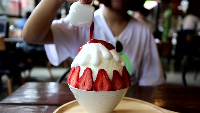 Closeup of Woman pouring strawberry into bingzu with milk snow ice on the table in restaurant