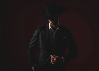 attractive young man wearing tuxedo and black hat on black background