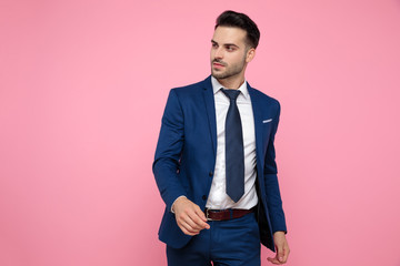 handsome casual man walking in navy blue suit on pink background