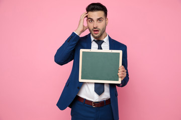 confused young man holding an empty board on pink background