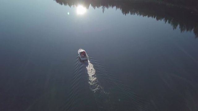 Beautiful aerial view of family in a boat moving slowly through Norwegian fjord with lull water reflecting the sunlight and islands, Camera tilting up to reveal the summer archipelago of Scandinavia