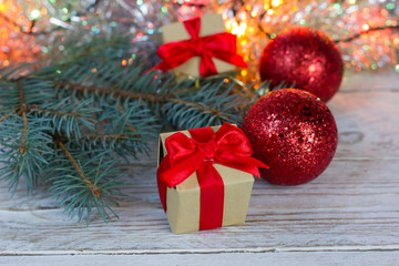 Fototapeta na wymiar Christmas Greeting Card. Gift with a red bow on a wooden table, fir branch, red Christmas balls. Bokeh