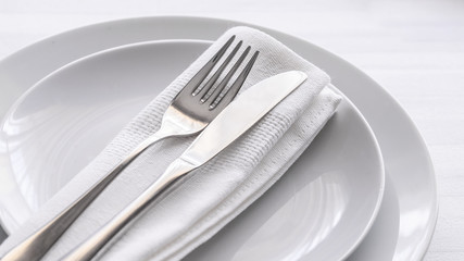 Close up of silverware fork and knife with napkin on white porcelaine plate. Copy space. Restaurant dinning concept.