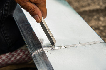 Closeup hand holding tin to solder gutter roof.