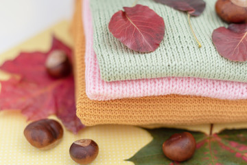 cosy autumn - knitted sweaters, chestnuts and autumn leaves on yellow background 