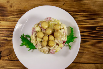 Potato salad with marinated mushrooms, sausage, onion and mayonnaise on wooden table