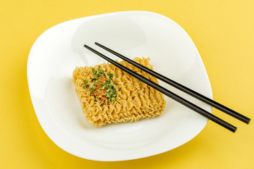A plate of noodles on a yellow background. Top view.