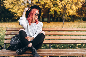 Naklejka na ściany i meble Pretty girl with red hair and hat relaxing on the bench in the park, autumn time.