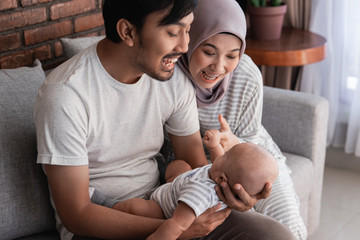 young asian family with infant son together smiling. muslim parenting