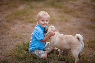 A boy with Down syndrome plays in the playground. Genetic disease in a child. Toddler hugs a dog.