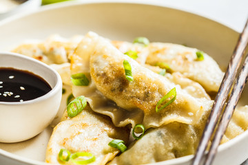 Fried Korean dumplings with green onion and sauce on white plate.