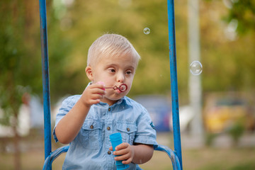 A child with Down cider plays in nature. Toddler blowing soap bubbles. Genetic abnormality in a boy.