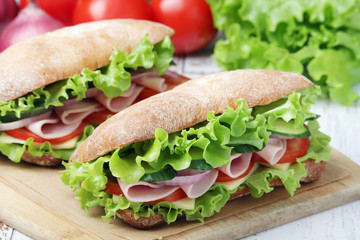 Two sandwiches with fresh vegetables, ham and cheese in ciabatta bread