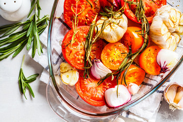 Baked tomatoes with garlic, onions and rosemary in glass oven dish, top view.