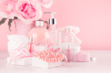 Elegant pink skin and body care products - cream, rose oil, liquid soap, salt, cotton towel - cosmetic accessories, romantic flowers  on white wood table.