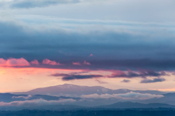 Obraz premium View of colorful clouds at sunset, over and below a mountain