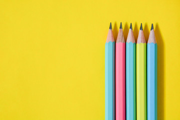 top view group of wooden pastel color pencils on yellow paper background with copy space, flat lay