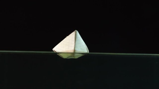 Paper boat floating in the water on a black background, slow motion, closeup