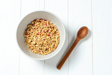 white wheat granola in a white bowl in a composition with a spoon on white wooden background. Healthy breakfast food. Making breakfast. Gluten free
