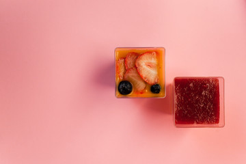 two juicy fresh desserts in cups pudding, chia seeds, mango puree, berries, multi-layer, panakota, passion fruit coconut milk on a pink background in isolated. copy space, place text