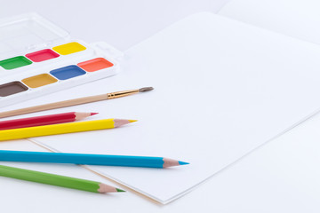 Creative design template from bright watercolor paints, brushes for drawing, colored pencils and an open album with blank pages for text or pictures. Side view. Mockup.