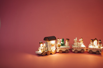 holiday magic concept.  New Year.  postcard.  small toy miniature white train with Santa, snowman, garland lights. Christmas tree, on pink background in isolation. Copy space. Place text. 