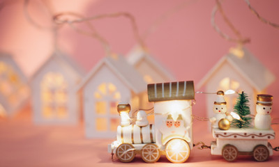 holiday magic concept.New Year. postcard.  small toy miniature white train with Santa, snowman, garland lights, Christmas tree,small houses luminous windows on pink background isolated. Place text