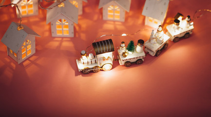 holiday magic concept.New Year. postcard.  small toy miniature white train with Santa, snowman, garland lights, Christmas tree,small houses luminous windows on pink background isolated. Place text
