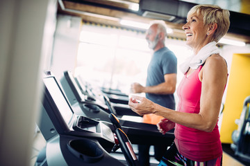 Senior people running on a treadmill in health club.