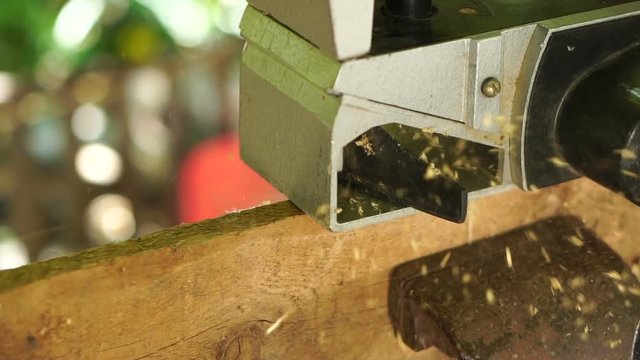 Carpenter using an electric planer processes the surface of the hedge, shavings fly beautifully to the side, slow motion, close-up