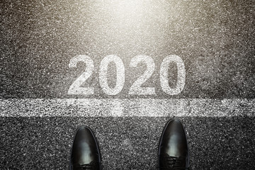 Businessman is looking down at his feet on a Asphalt road with 2020 number painted on the surface.Concept for success in the future goal and passing time. Happy new year