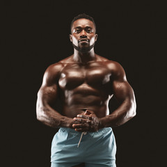 Fototapeta na wymiar Portrait of muscular sportsman demonstrating his body over black background