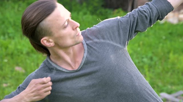 An average plan a young man in Indian clothes and pants Aladdin practices qigong while doing exercises while working with qi energy outdoors in summer next to an old hut
