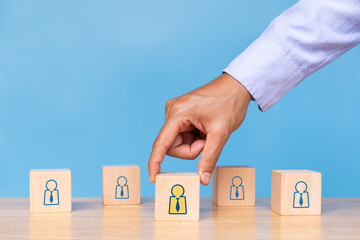 businessman hold wooden cube with choose human icon on blue background. Concept of human resources management and recruitment business