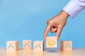 Businessman hold wooden cube with smiley face icon on blue background. Service rating, satisfaction concept