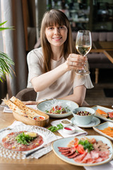 Portrait of a beautiful young elegant woman in the restaurant with a wine glass. Dinner and a variety of dishes on the table. Italian cuisine