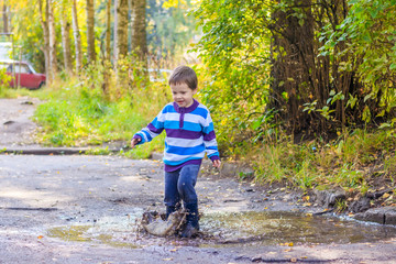 A little boy is jumping in a puddle. A boy in rubber boots. Happy childhood. Puddles after the rain. Warm summer evening.