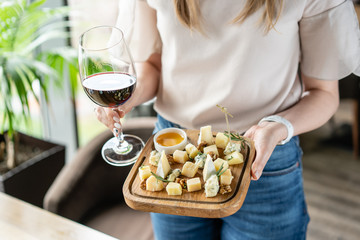 Girl holding glass red wine and wooden plate with cheese. Delicious cheese mix with walnuts, honey....